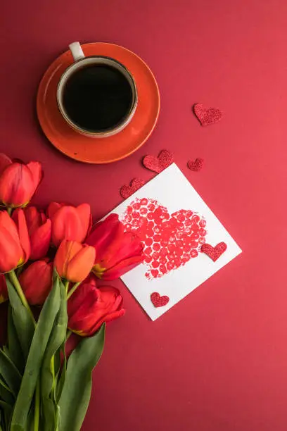 Photo of morning coffee and a bouquet of red tulips on a bright red background. View from above.Copy space for text. The concept of holidays.