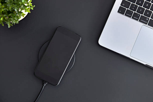 istock Recharging smartphone battery using round induction wireless charger. Top down view of office workplace. 1326396039