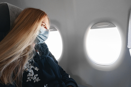 Blonde woman in medical mask sitting in the plane by the window close up