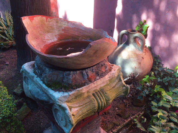 This group of objects seen on a cemetery in Rome is a sort of antique still life of forgotten objects. A stand, an old jug and a broken pot or vase filled with water in front of a pink wall.