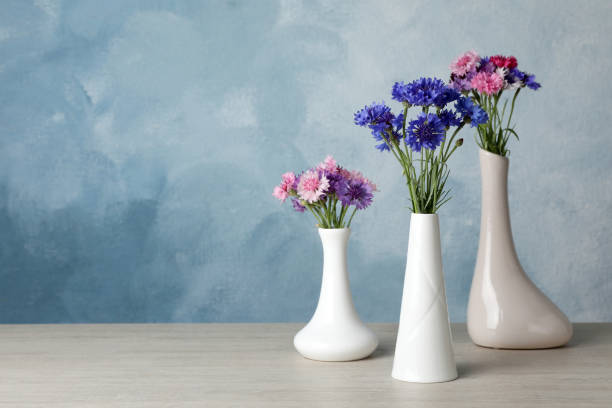 istock Beautiful cornflowers in vases on white wooden table. Space for text 1326400581