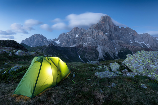 Dusk in mountain landscape with illuminated tent. Mountain peaks, Dolomites, Italy. Illuminated tent high in the mountains under the night sky Hiking and climbing concept