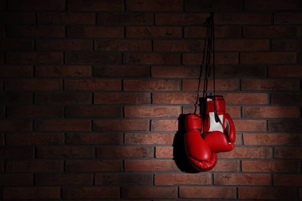 istock Pair of red boxing gloves hanging in spotlight on brick wall, space for text 1326400918