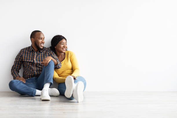 istock Young African Couple Sitting Near Wall In Empty Flat And Looking Aside 1326401038