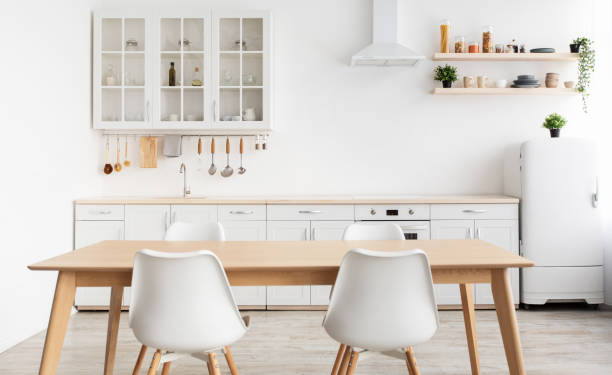 istock Modern design scandinavian kitchen. White kitchen furniture and dining table with chairs, utensils and kitchenware 1326401087
