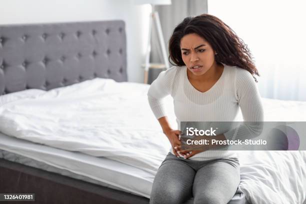 Woman With Right Side Pain Sitting On Bed At Home Stock Photo - Download Image Now - Liver - Organ, Pain, Urinary Tract Infection