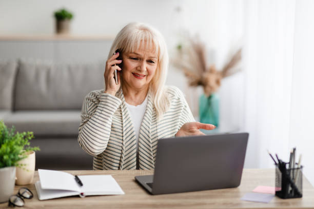 istock Confused mature woman talking on mobile phone using laptop 1326402351