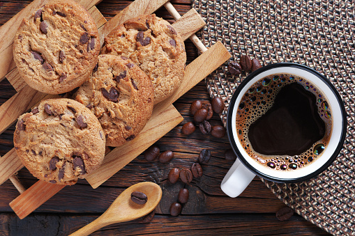 Cup of coffee and chocolate chip cookies on wooden table close up, top view