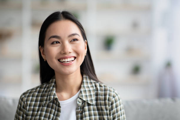 istock Joyful young asian lady sitting on couch at home 1326403409