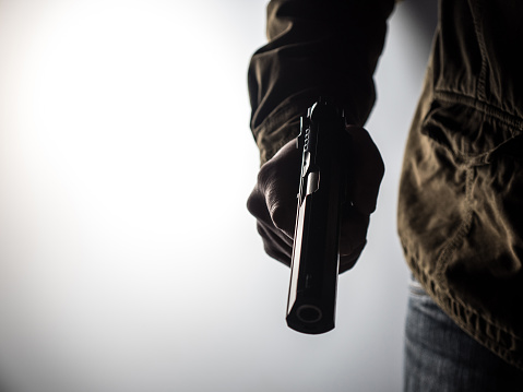 High contrast image of a man holding a gun against a brightly lit background