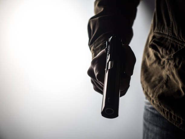 Man holding a gun High contrast image of a man holding a gun against a brightly lit background gunman photos stock pictures, royalty-free photos & images