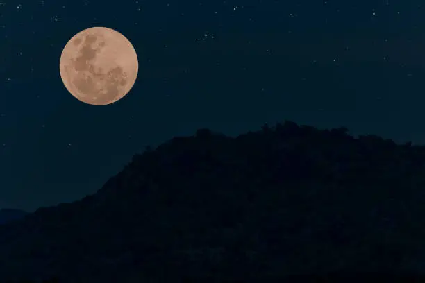 Photo of Full moon on the sky with mountain silhouette at night.
