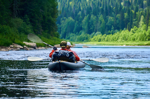 couple of tourists in a two-seater kayak rafting down the river among the mountains