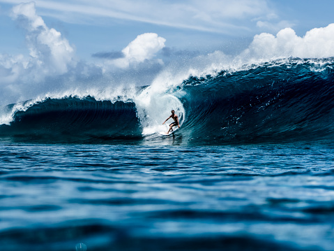 A surfer surfing a wave, blue and big wave in Teahupo’o, French Polynesia