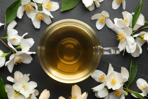 tasse en verre de thé au jasmin et fleurs fraîches sur table noire, pose plate - jasmine tea black tea tea drink photos et images de collection