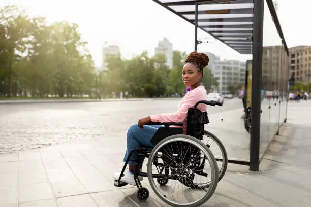 Photo of Young black handicapped woman in wheelchair cannot board vehicle suitable for impaired persons, waiting on bus stop