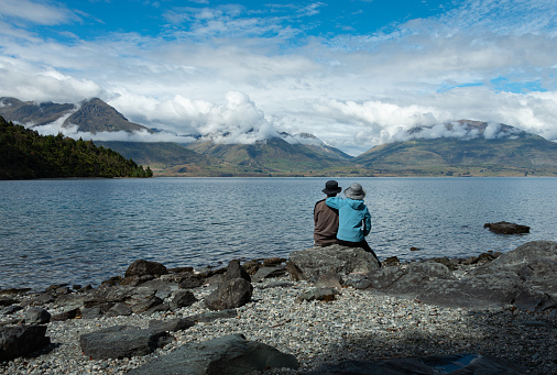 Two people sitting on the rocks, enjoying the mountain views across Lake Wakatipu, Queenstown.