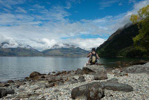 A man sitting on the rocks, enjoying the mountain views across Lake Wakatipu, Queenstown