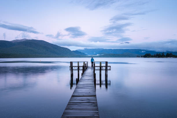 donna solitaria in piedi alla fine del molo del lago te anau all'alba, guardando le montagne keplero. formato orizzontale. - te anau foto e immagini stock