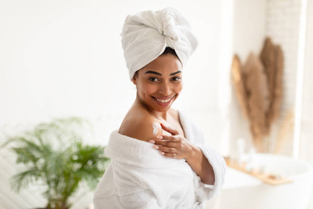 istock Black Woman Applying Lotion On Shoulder Standing In Modern Bathroom 1326414226