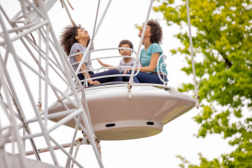 A Cheerful Family of African-American Ethnicity is Spending the Time Together and Riding on a Ferris Wheel in Large Amusement Park.