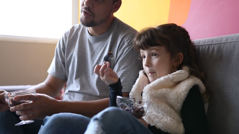 Father and Daughter eating sweets and watching TV