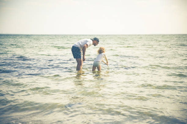 Father and danish girl with blond hair having fun outdoors in nature while catching sea critters on the beach with a children's fishing net. This scene is the new normal that comes with a flexible job or freelancer while homeschooling kids.