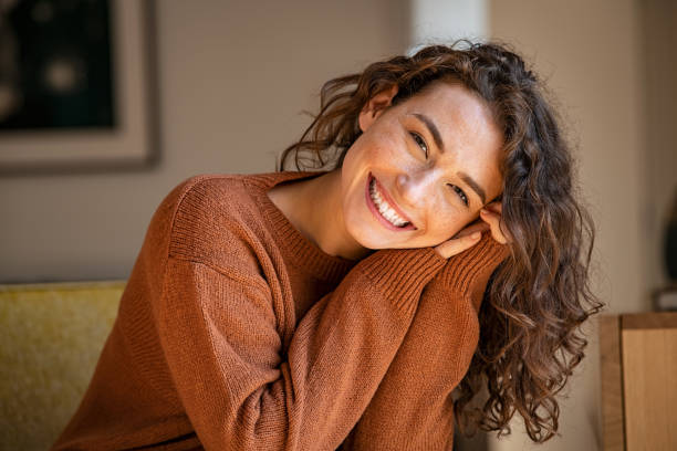 Young woman laughing while relaxing at home Happy young woman sitting on sofa at home and looking at camera. Portrait of comfortable woman in winter clothes relaxing on armchair. Portrait of beautiful girl smiling and relaxing during autumn. one woman only stock pictures, royalty-free photos & images