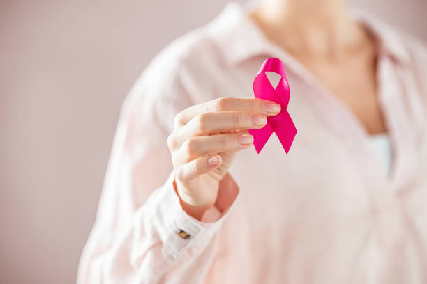 Woman holding pink breast cancer ribbon Close up of woman holding pink ribbon for breast cancer awarness. Detail of female hand holding pink awareness ribbon. Young woman supporting living with women's breast tumor. research foundation stock pictures, royalty-free photos & images