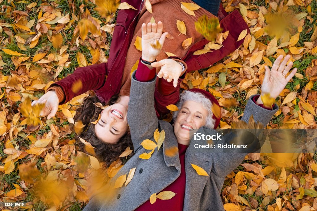 Nonna e nipote sdraiate sul fogliame e godersi l'autunno - Foto stock royalty-free di Autunno