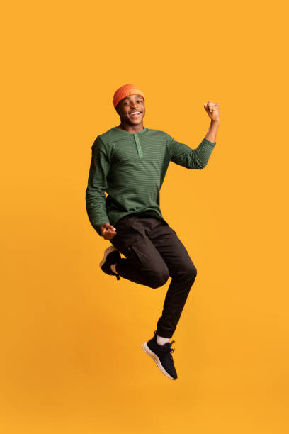 célébrer le succès. émotionnel jeune gars noir sautant dans les airs avec les poings serrés - hip hop hipster afro men photos et images de collection