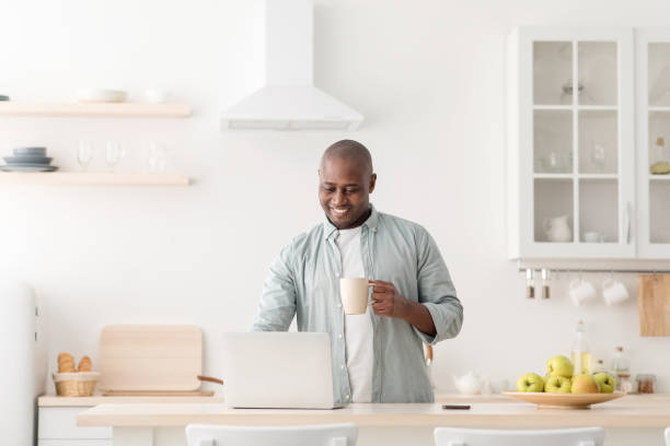 istock Modern worker in self-isolation. Happy mature african american man with cup, drinking coffee and working on laptop 1326420507