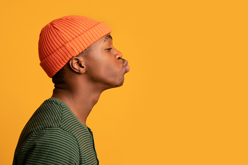 Retrato de perfil de joven negro con sombrero naranja enviando beso de aire photo