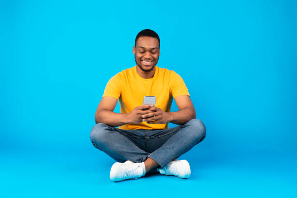 istock Happy Black Man Using Mobile Phone Sitting Over Blue Background 1326420639