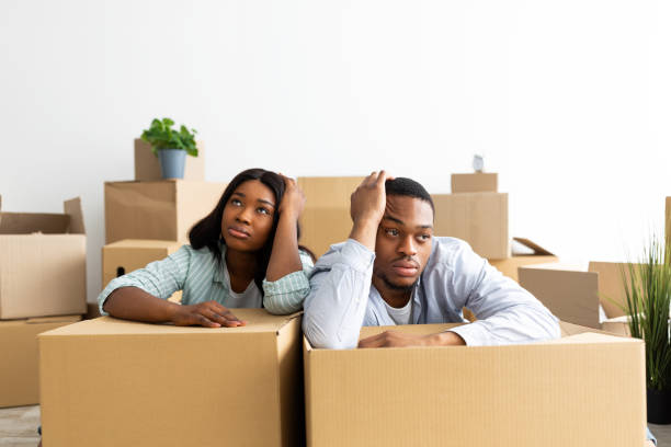 pareja negra triste y cansada apoyada en cajas desempaqueadas, sentada en la habitación llena de cajas, lista para mudarse a una nueva casa - moving house physical activity real estate couple fotografías e imágenes de stock