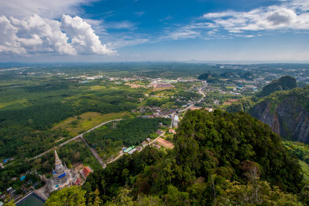 View from the cliff to the Tiger Cave temple and green fields. Small houses in the distance. Clouds in the blue sky. View from the cliff to the Tiger Cave temple and green fields. Small houses in the distance. Clouds in the blue sky. wat tham sua stock pictures, royalty-free photos & images
