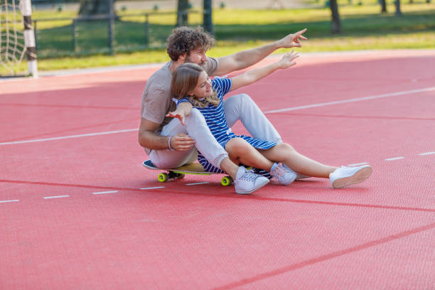 istock Young Father is Having Fun With his Daughter While They Riding a Skateboard Together. 1326421112