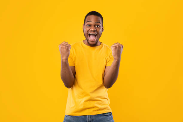 ragazzo afroamericano gesticolare sì gridando pugni tremanti, sfondo giallo - shaking fist foto e immagini stock