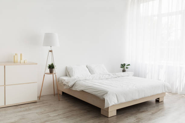 シンプルなモダンなデザイン、広告、提供。白い枕と柔らかい毛布、ランプ、木製の床に家具が付いているダブルベッド