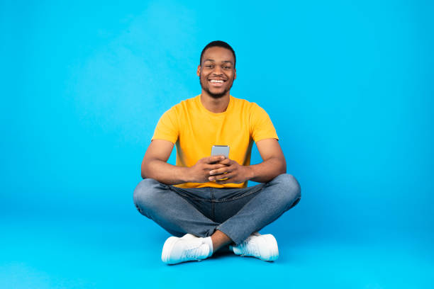 istock Happy african american male using cellphone sitting on blue background 1326421877