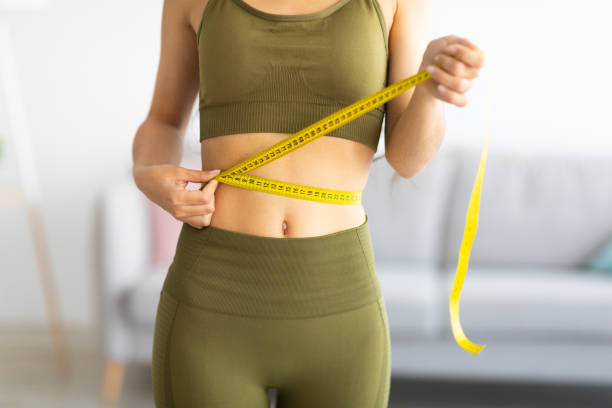 cropped view of slim indian woman measuring her waist with tape measure at home, closeup - east asian ethnicity imagens e fotografias de stock