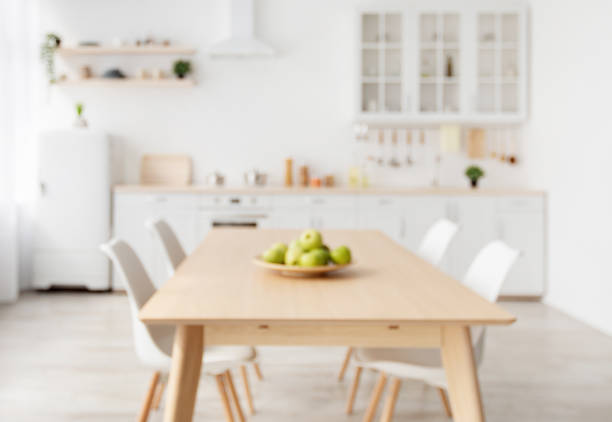 istock Blurred background with modern light kitchen, wooden dining table and white furniture, chairs, kitchenware and utensils 1326422284