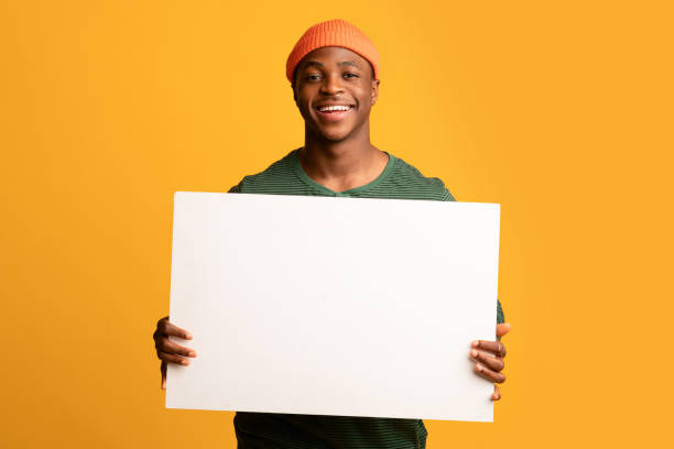 istock Cheerful Black Guy Holding White Blank Placard While Posing Over Yellow Background 1326425037