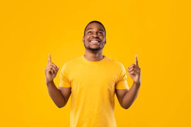 istock Cheerful Black Guy Pointing Fingers Up Posing Over Yellow Background 1326425100