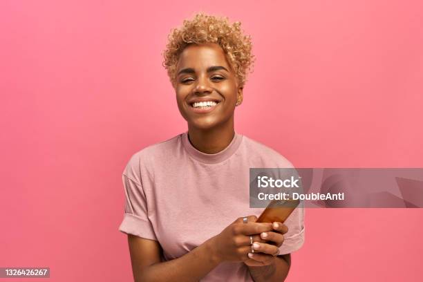 Half Length Shot Of Positive Attractive Female Model With Afro Haircut Feels Good Uses Smartphone Device For Entertainment And Online Chatting Surfers Social Network Profile Uses Free Internet Stock Photo - Download Image Now