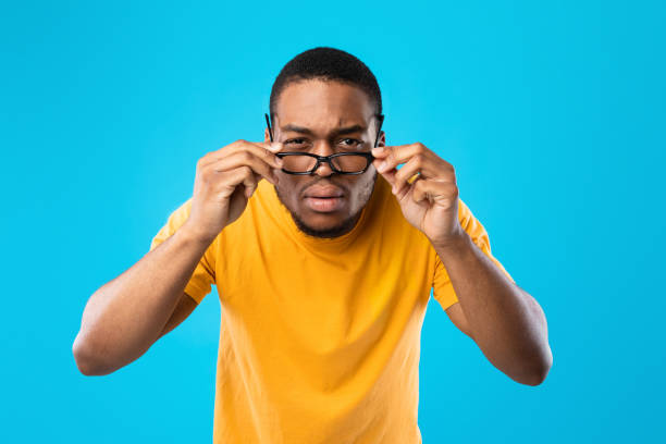 hombre afroamericano entrecerrando los ojos mirando a través de anteojos, fondo azul - entrecerrar los ojos fotografías e imágenes de stock