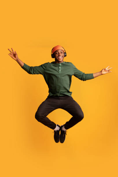 portrait de joyeux joyeux heureux noir gars dans des écouteurs sans fil sautant dans l’air - hip hop hipster afro men photos et images de collection