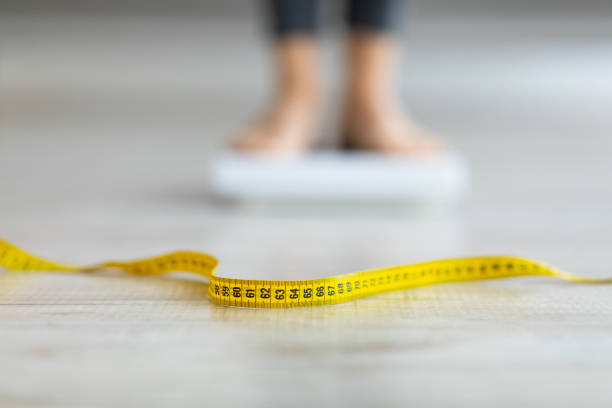 Measuring tape on floor and blurred view of millennial woman on scales, checking result of her slimming diet Measuring tape on floor and blurred view of millennial woman on scales, checking result of her slimming diet, selective focus. Healthy living, weight control concept. Copy space chubby arab stock pictures, royalty-free photos & images