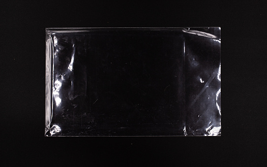 Transparent sealed plastic envelope on a black background, disposable glossy polyethylene bag