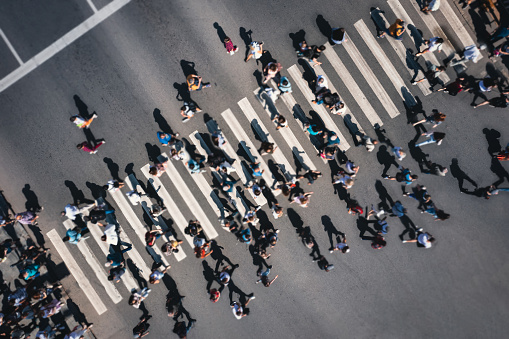 Different blurred people at a pedestrian crossing in the city - drone shot. People at a zebra pedestrian crossing - a lot of pedestrians in an overcrowded city on a sunny day. Aerial drone shot.